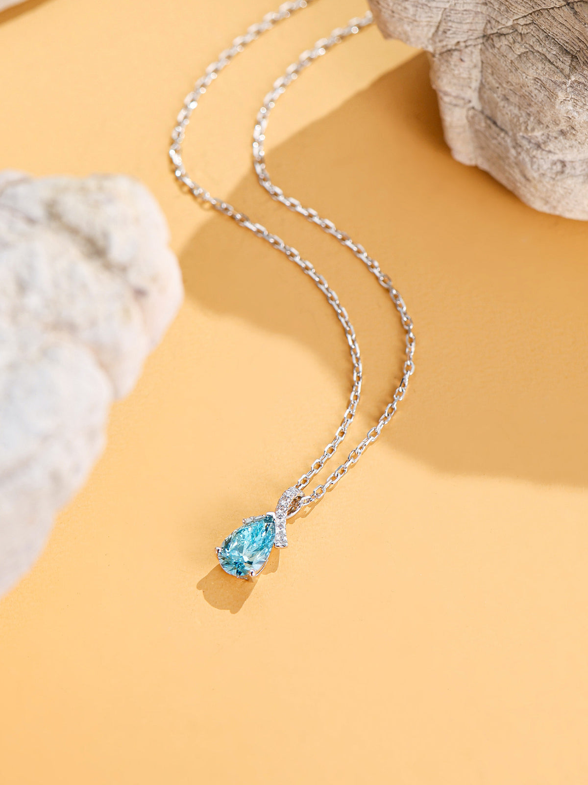 DANFÉE Ribbon Bow Pear blue diamond necklace on a warm sand backdrop