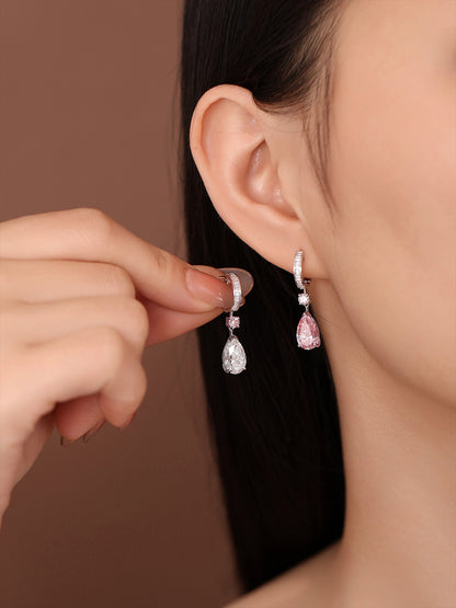 Model holding the white pear earring next to the pink pear earring she is wearing