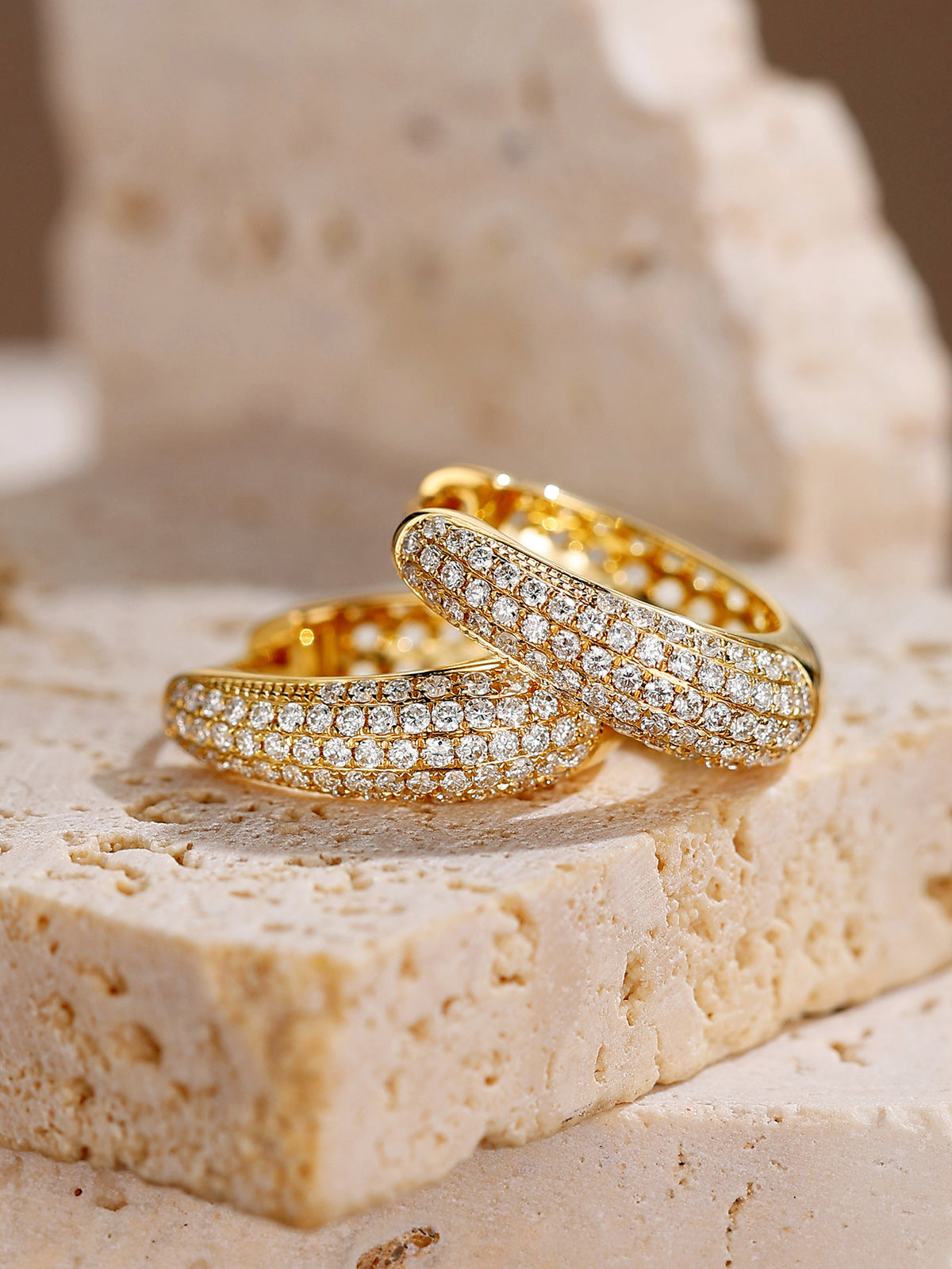 Pavé diamond huggie hoops in 18K yellow gold on travertine
