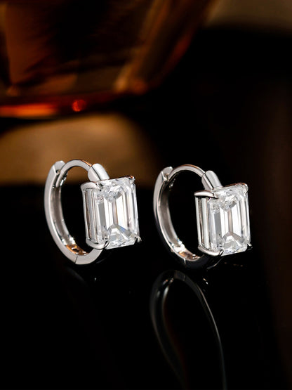 Emerald-cut diamond huggie earrings on a dark reflective surface