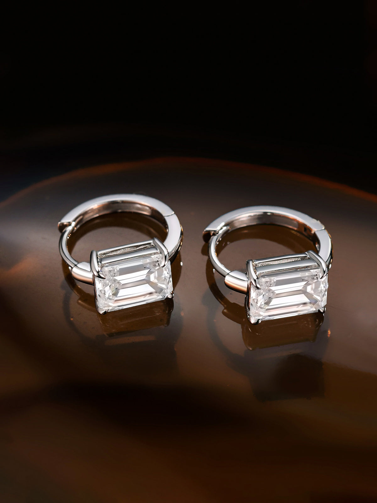 Emerald-cut diamond huggie hoops in warm amber light