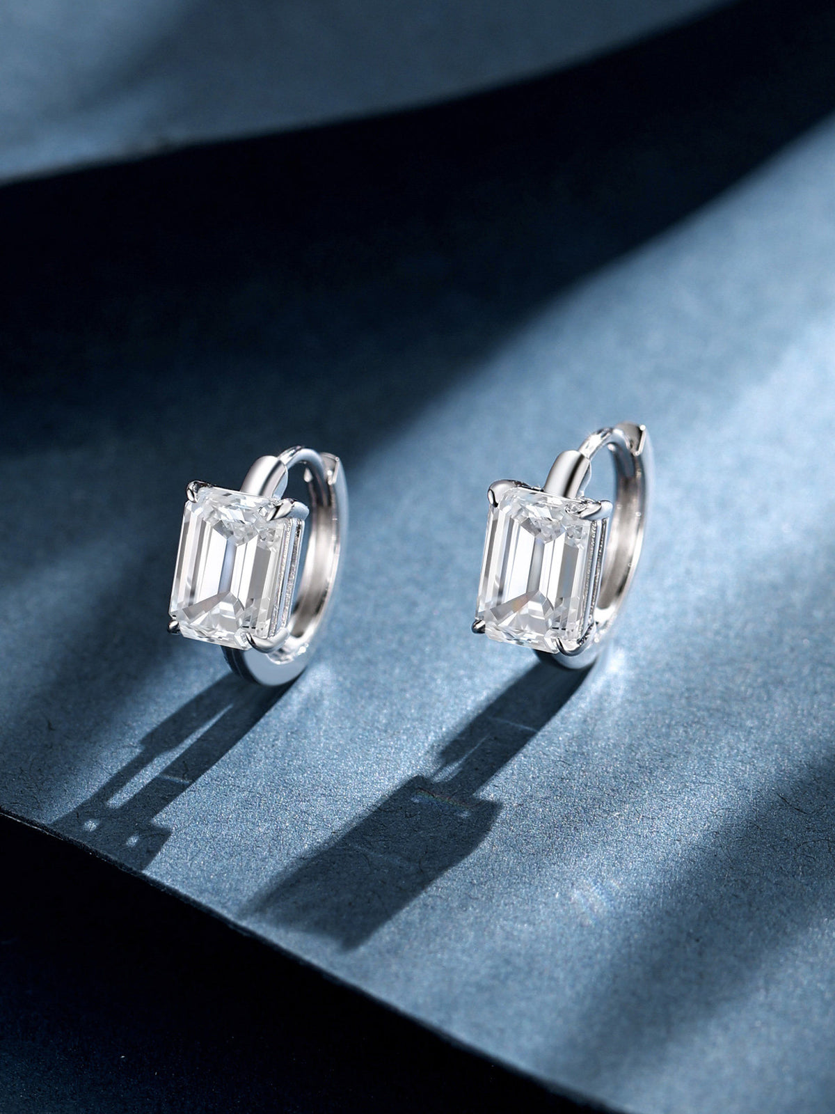 Emerald-cut lab-grown diamond huggie earrings on blue paper with shadow