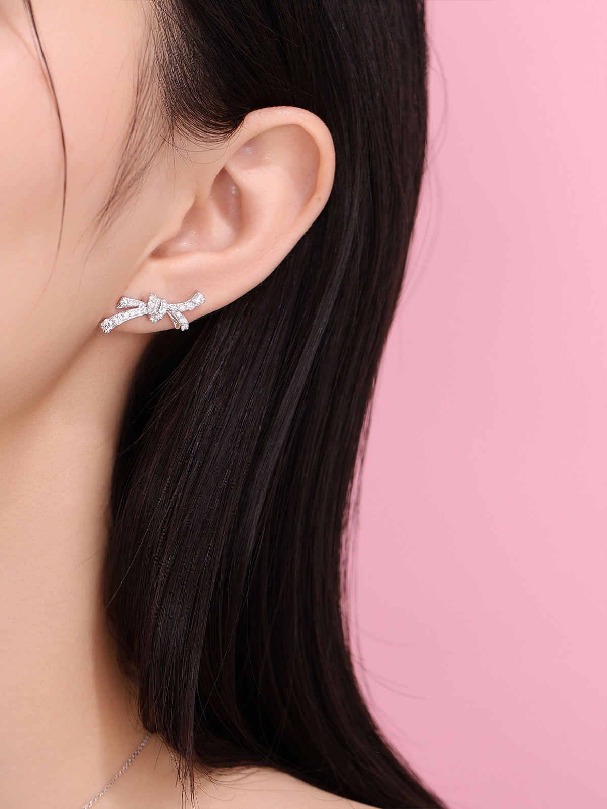 Diamond bow earring worn against a pink background