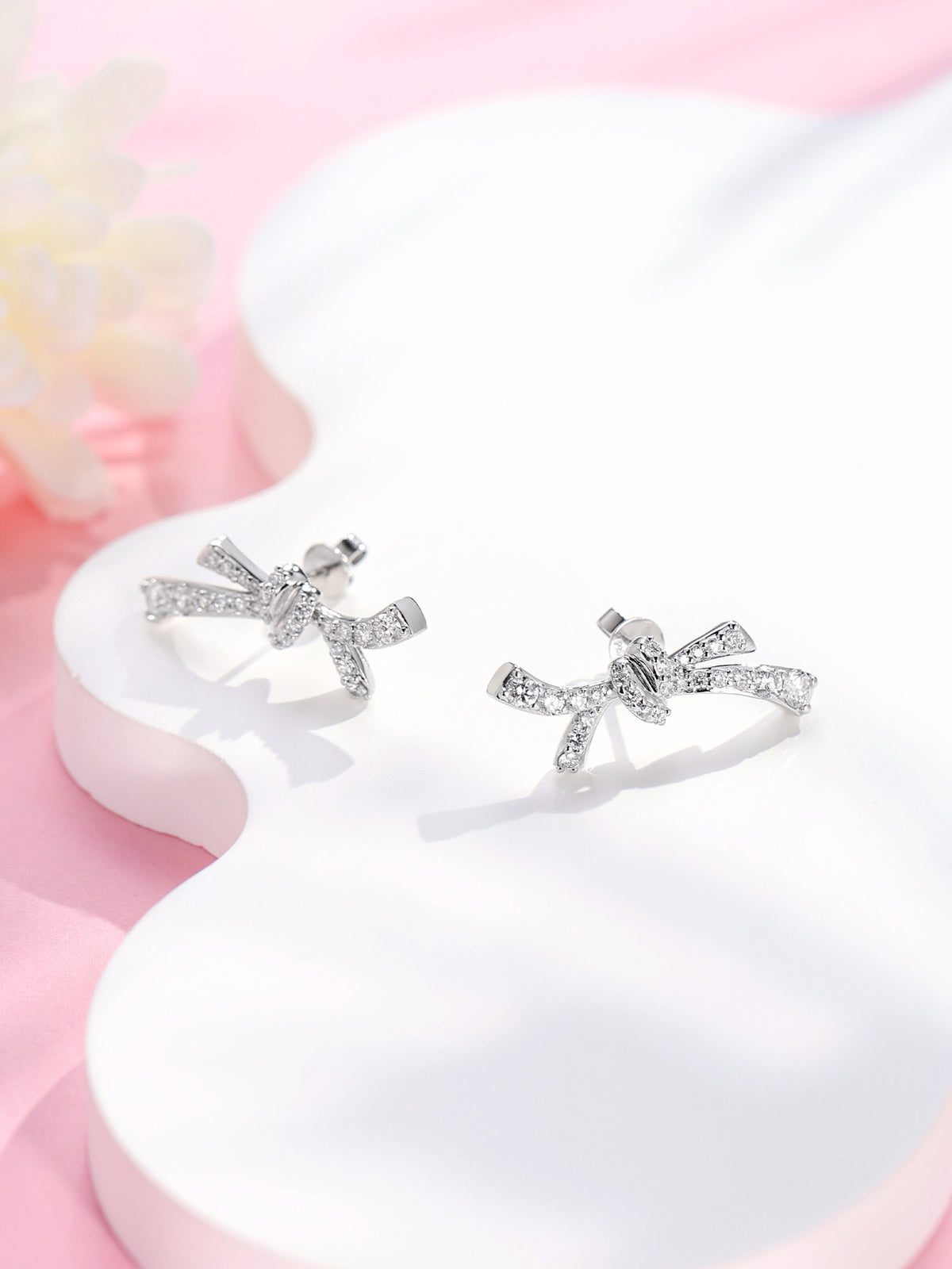 Diamond bow stud earrings in platinum on a pink and white display