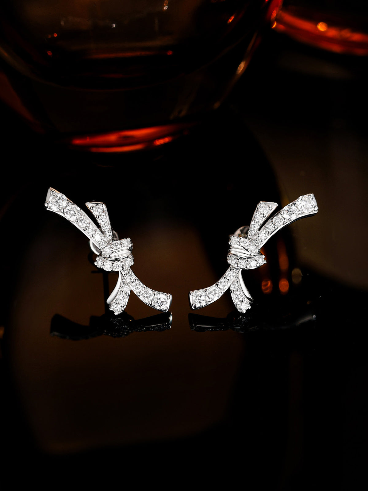Diamond bow stud earrings sparkling against a dark amber background