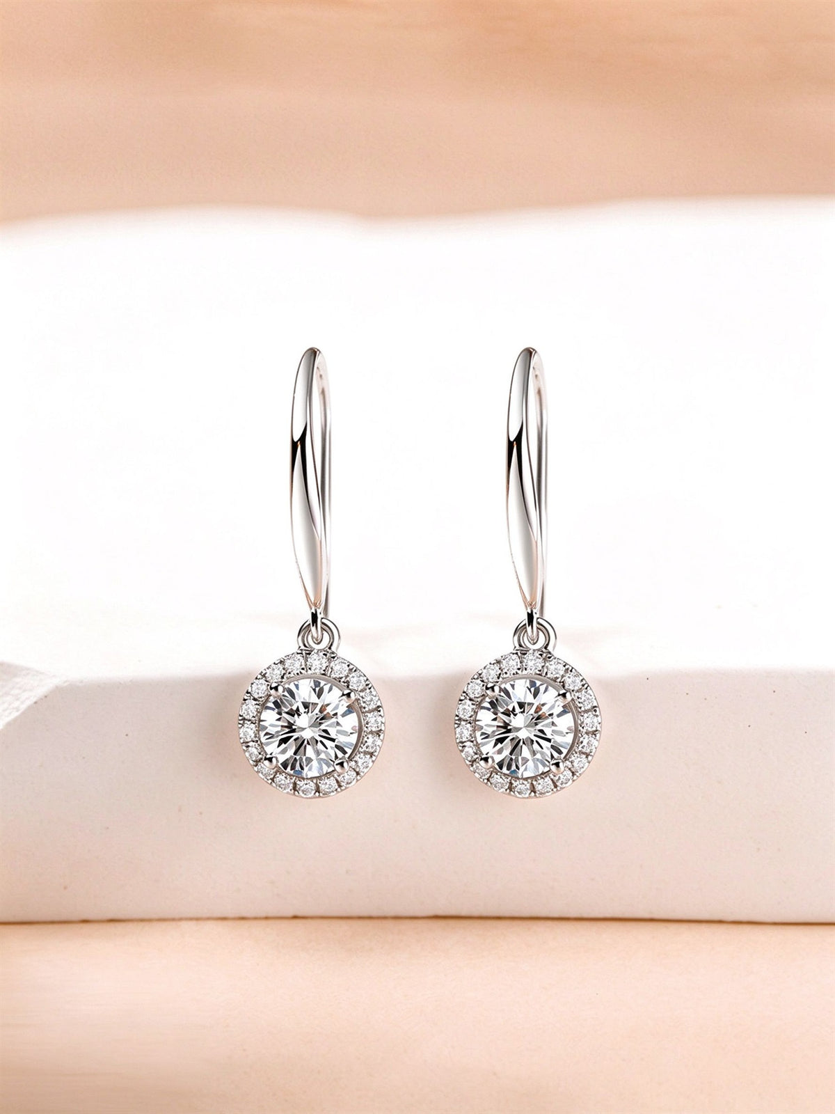 Round halo diamond drop earrings on French hooks, displayed on a white stone block