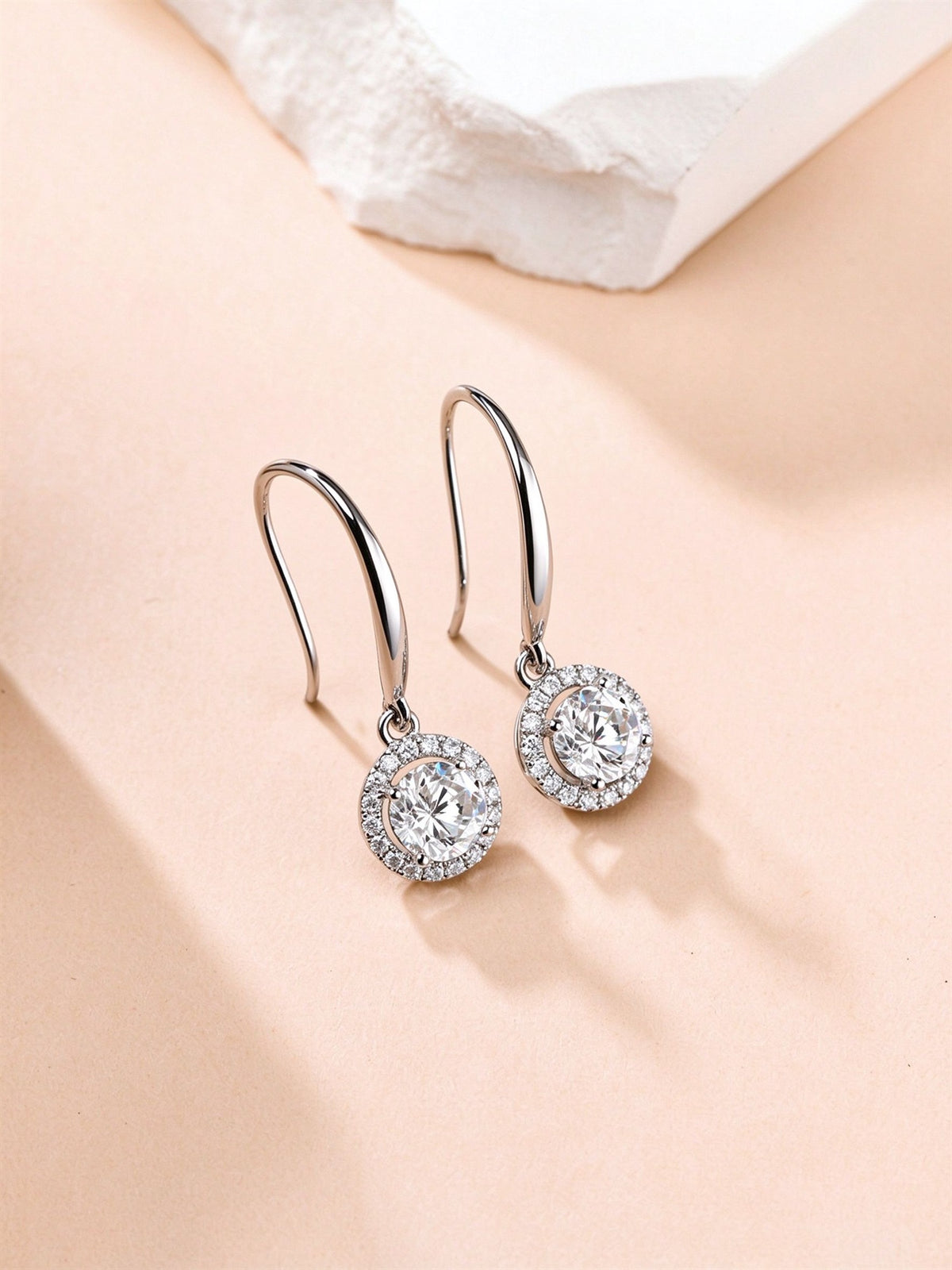 Lab-grown diamond halo drop earrings resting on a blush backdrop