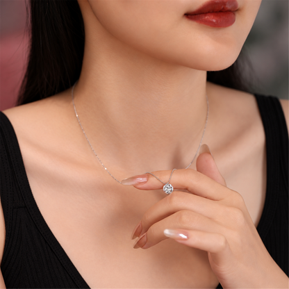 Round solitaire diamond pendant held at the neckline with a black top; edited supplier styling photo