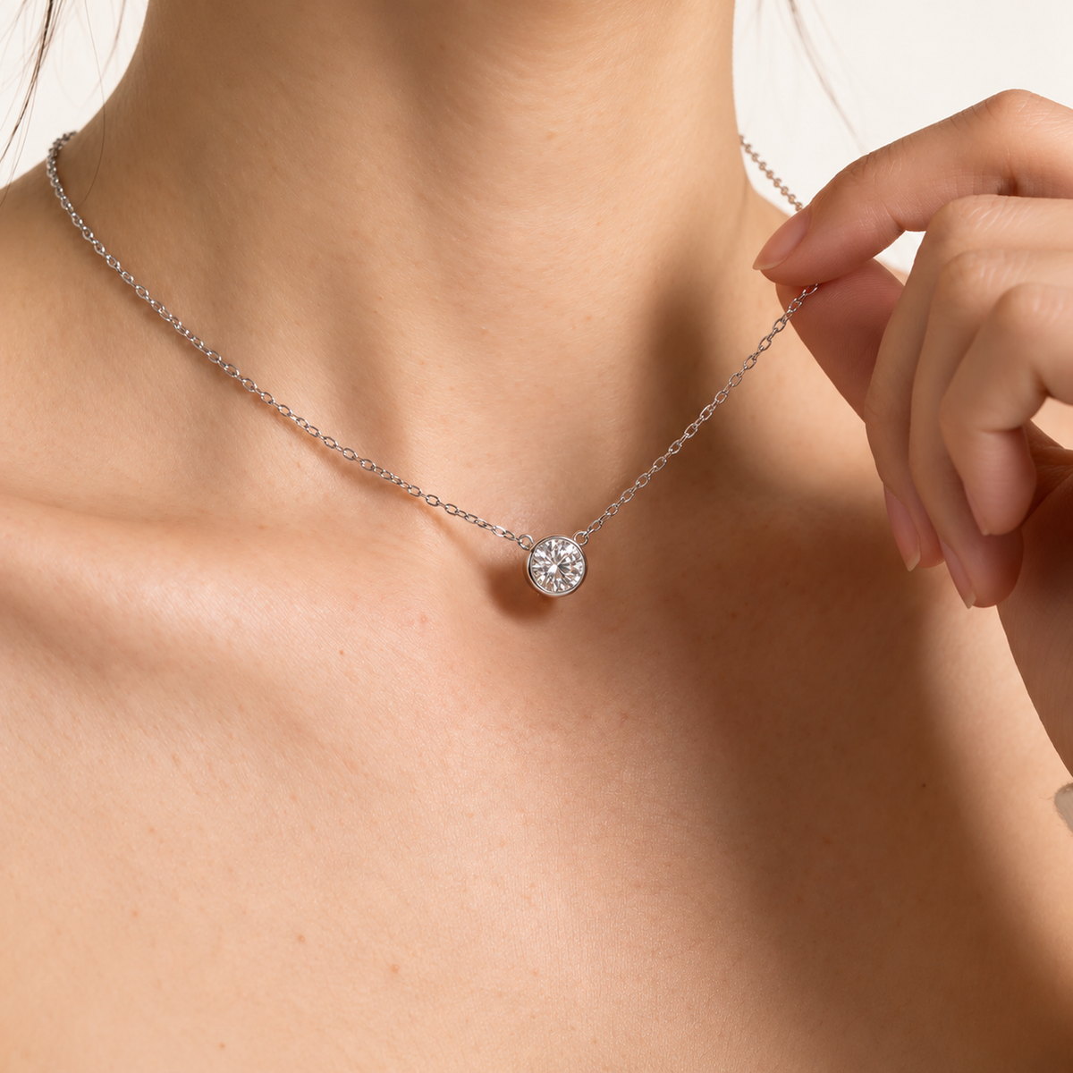 White gold bezel diamond necklace worn at the neckline, hand holding the chain