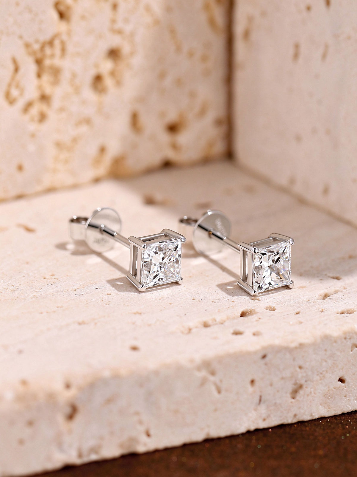 Princess-cut diamond solitaire studs in 18K white gold on travertine stone
