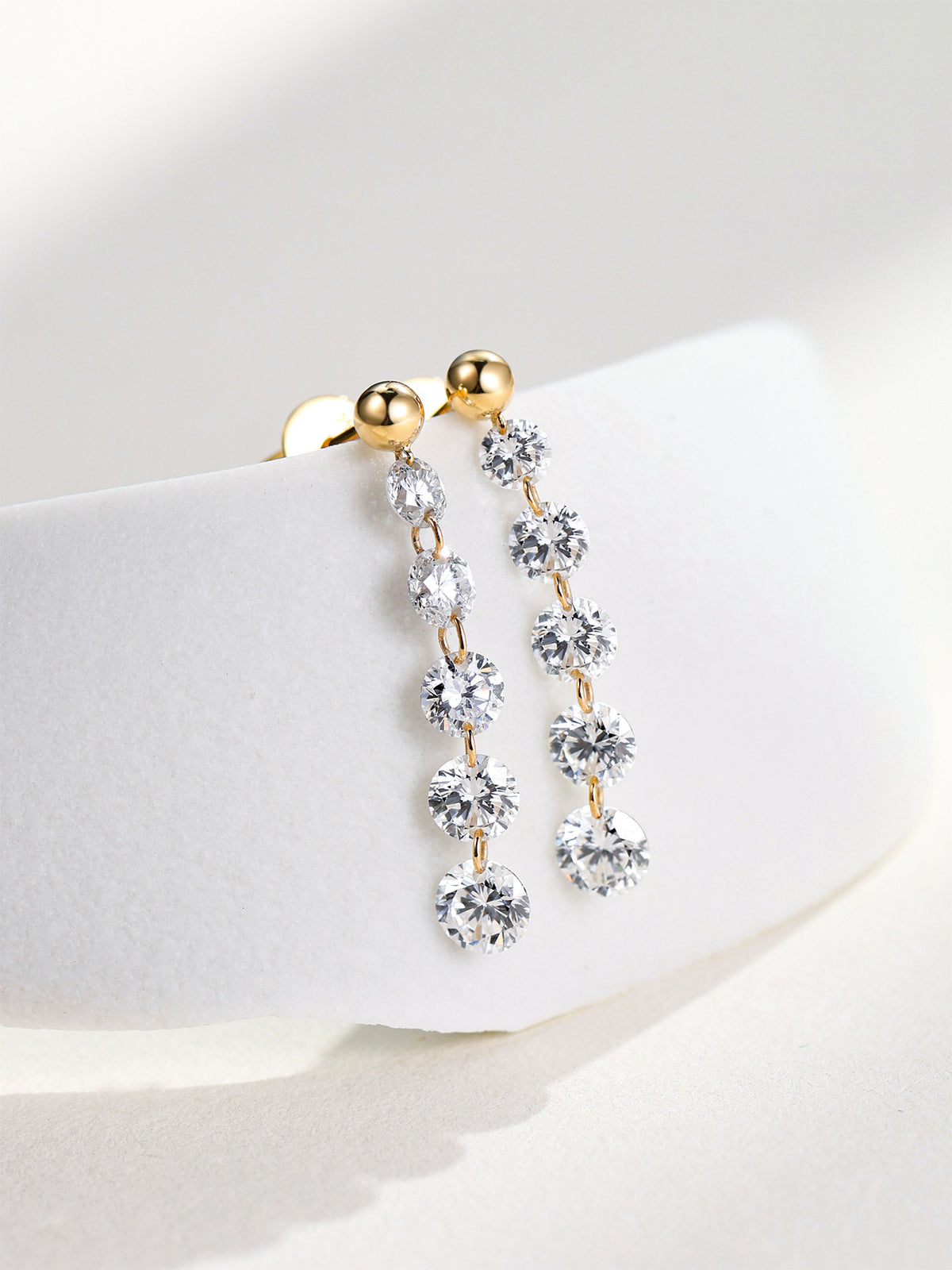 18K gold graduated diamond drop earrings displayed on white stone