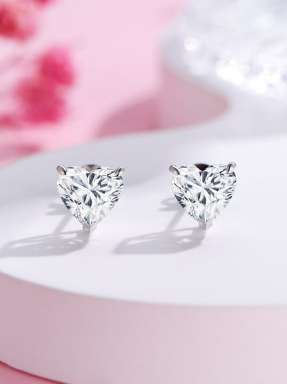 Three-prong heart-cut lab-grown diamond stud earrings on a pink backdrop