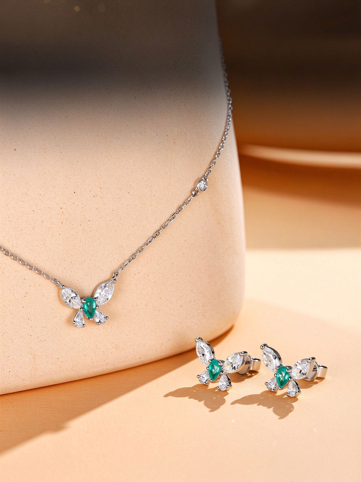 Éclair butterfly diamond stud earrings styled with matching butterfly pendant on warm sandstone