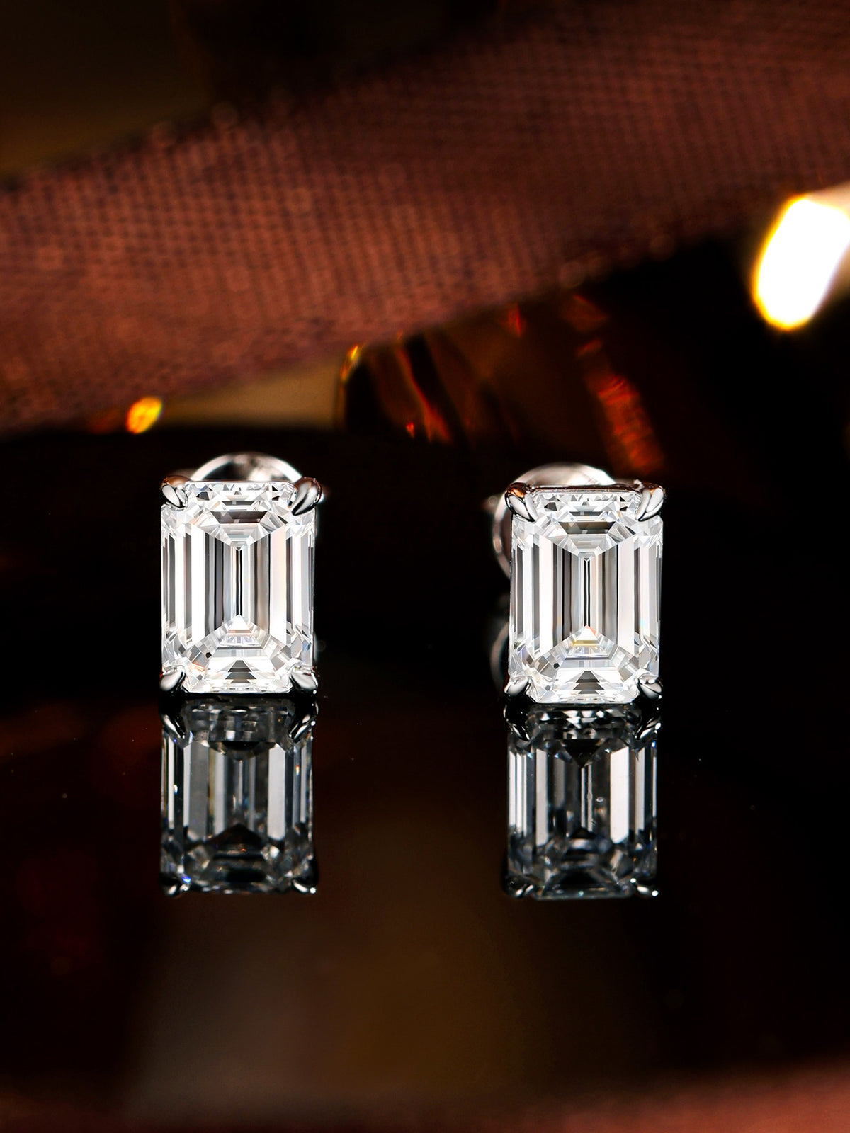 Emerald-cut lab-grown diamond solitaire studs reflected on a dark mirror