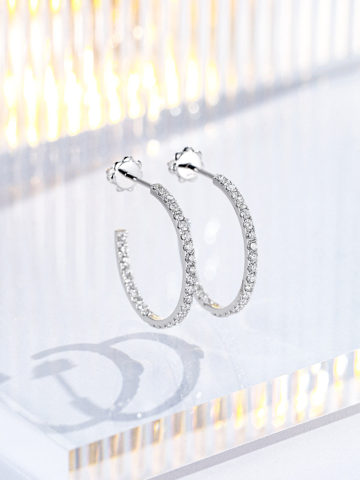 Pair of 20mm 18K white gold diamond hoop earrings with flower-shaped push backs on acrylic