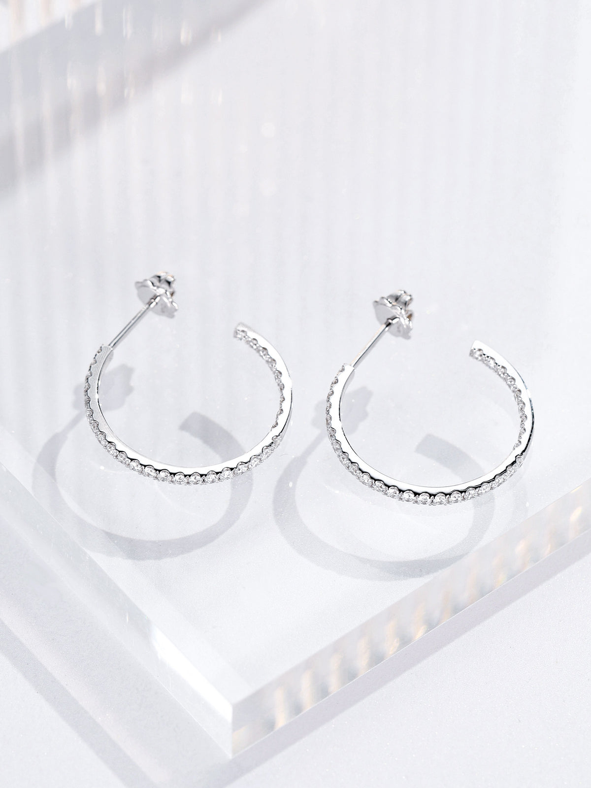 Open hoop earrings set with round lab-grown diamonds inside and out, lying flat