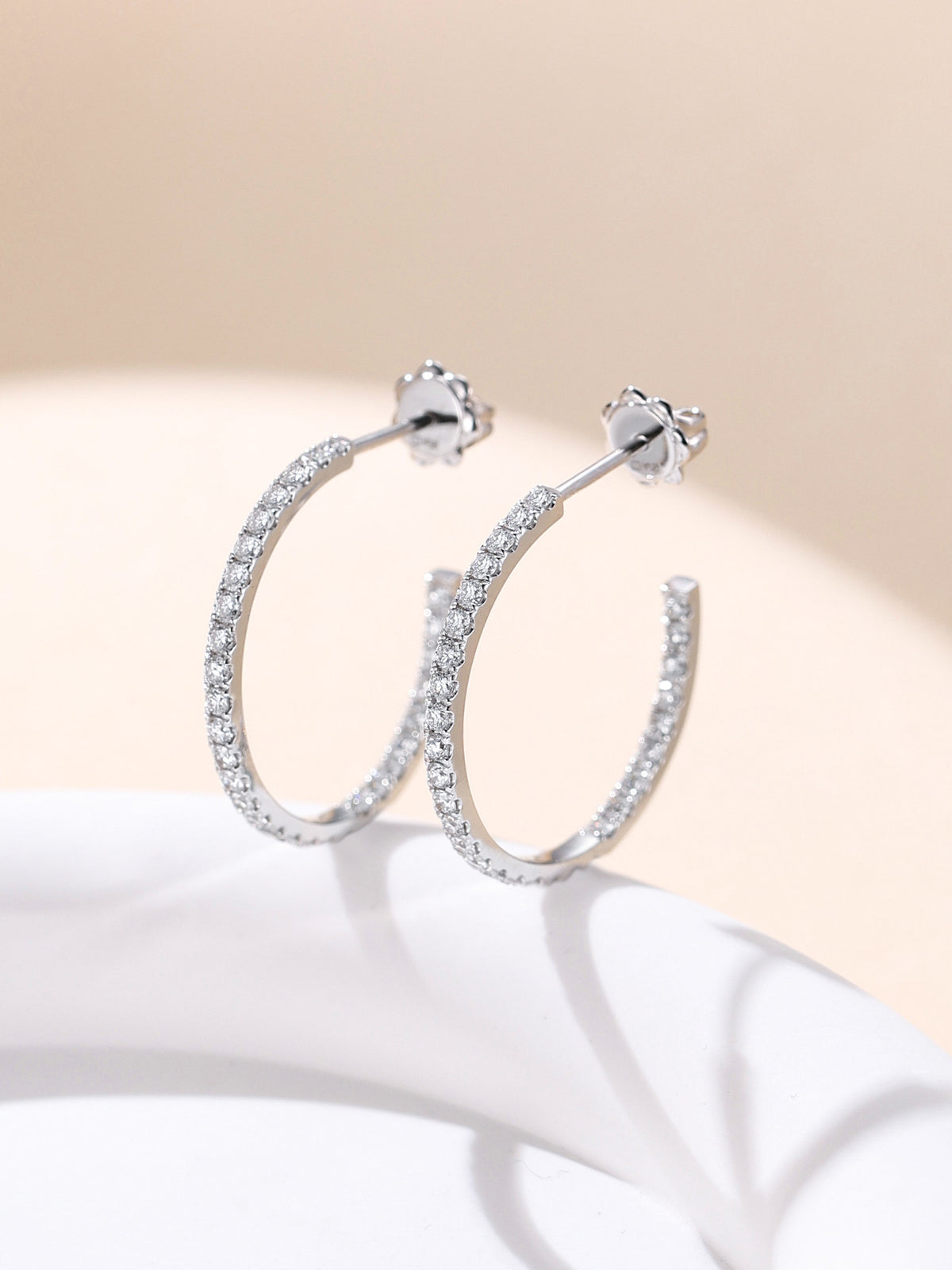 18K gold inside-out diamond hoop earrings standing on a white pedestal