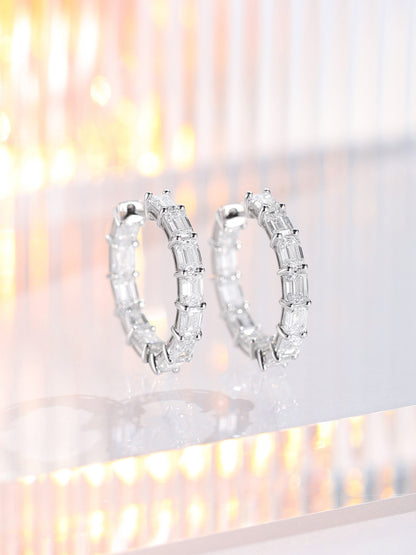 Pair of emerald-cut lab-grown diamond hoop earrings in platinum standing on acrylic with warm light