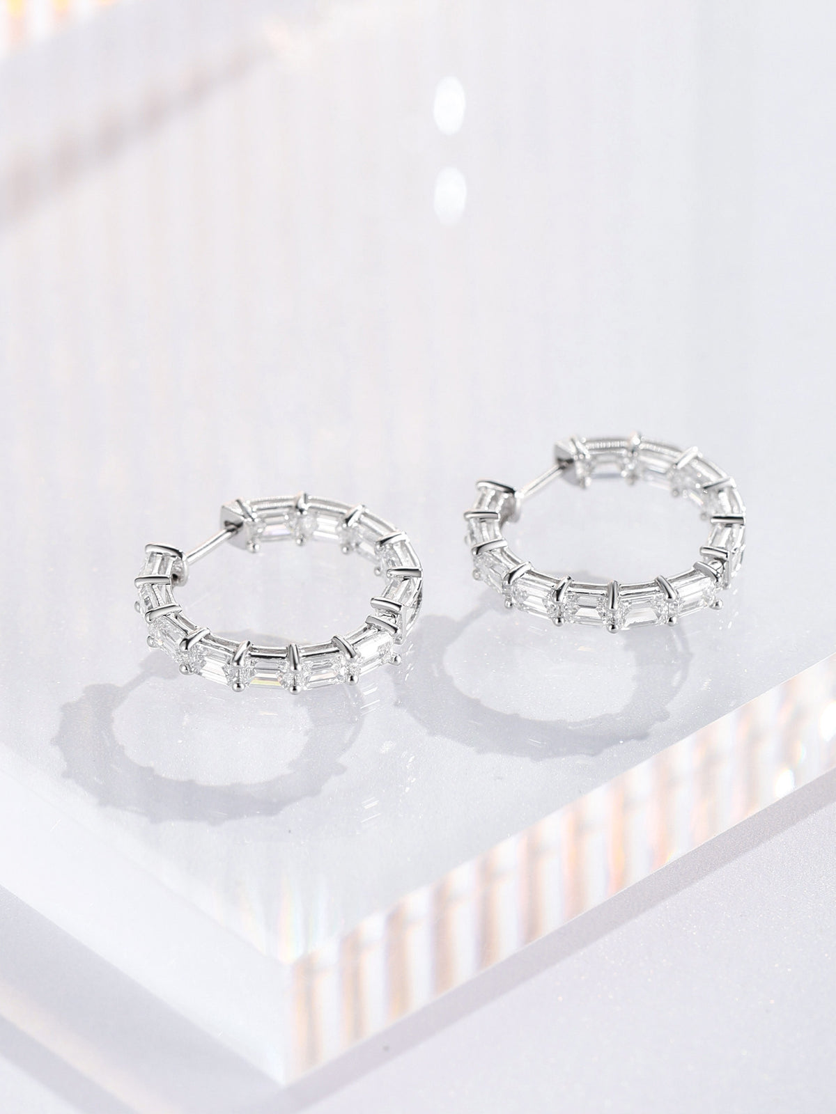 PT950 platinum inside-out diamond hoop earrings lying on a clear acrylic block