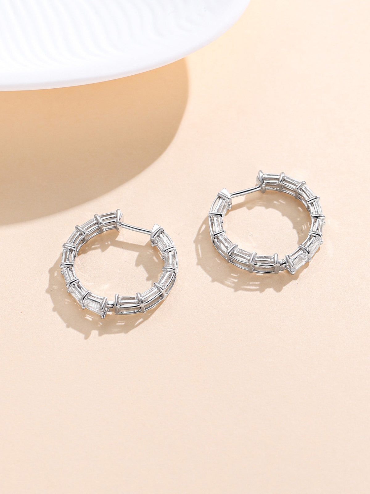Emerald-cut diamond hoop earrings with hinged snap closure on a beige background