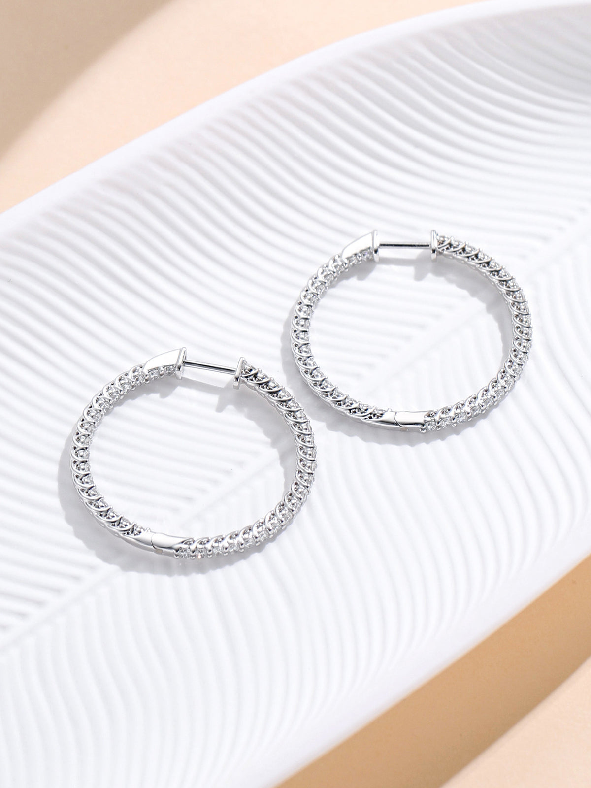 Inside-out diamond hoop earrings resting on a white leaf dish