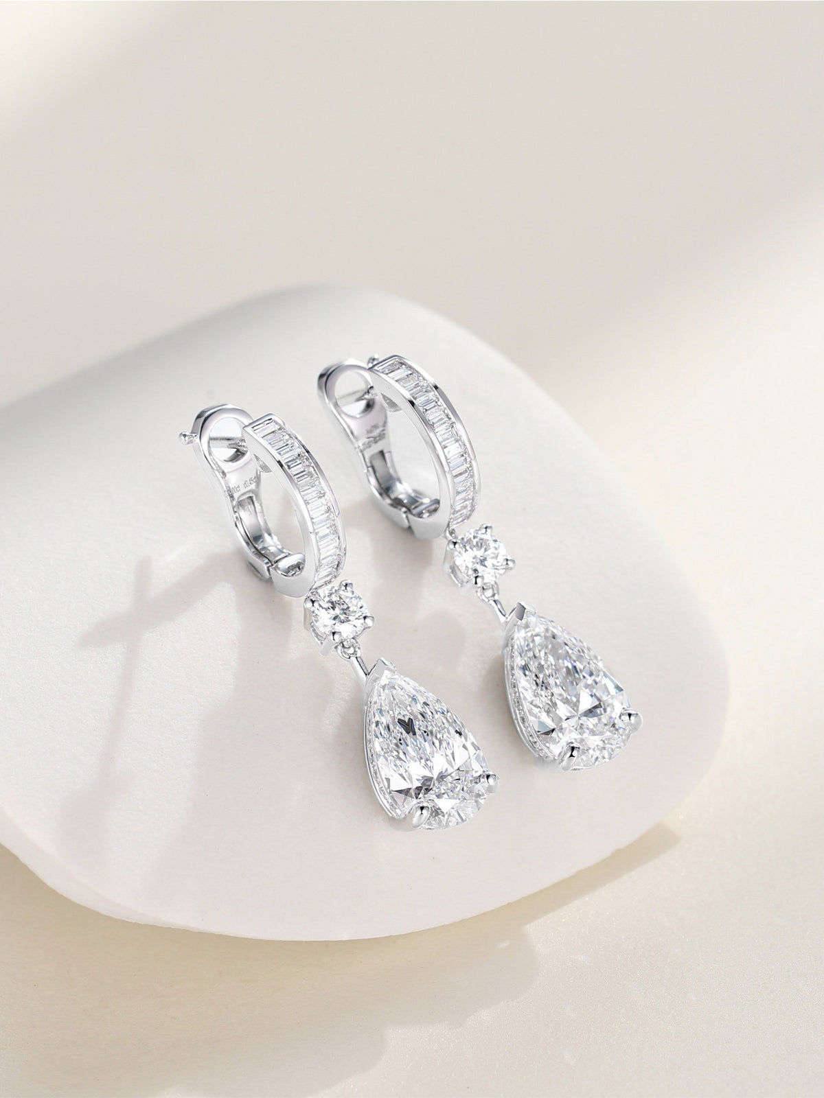 Pair of pear-cut lab-grown diamond drop earrings in 18K white gold resting on a white stone