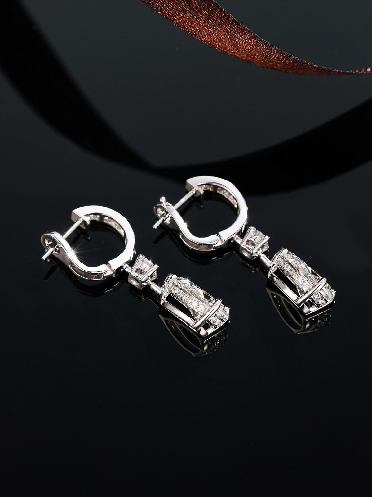 18K white gold huggie drop earrings with omega clip backs on a black reflective surface