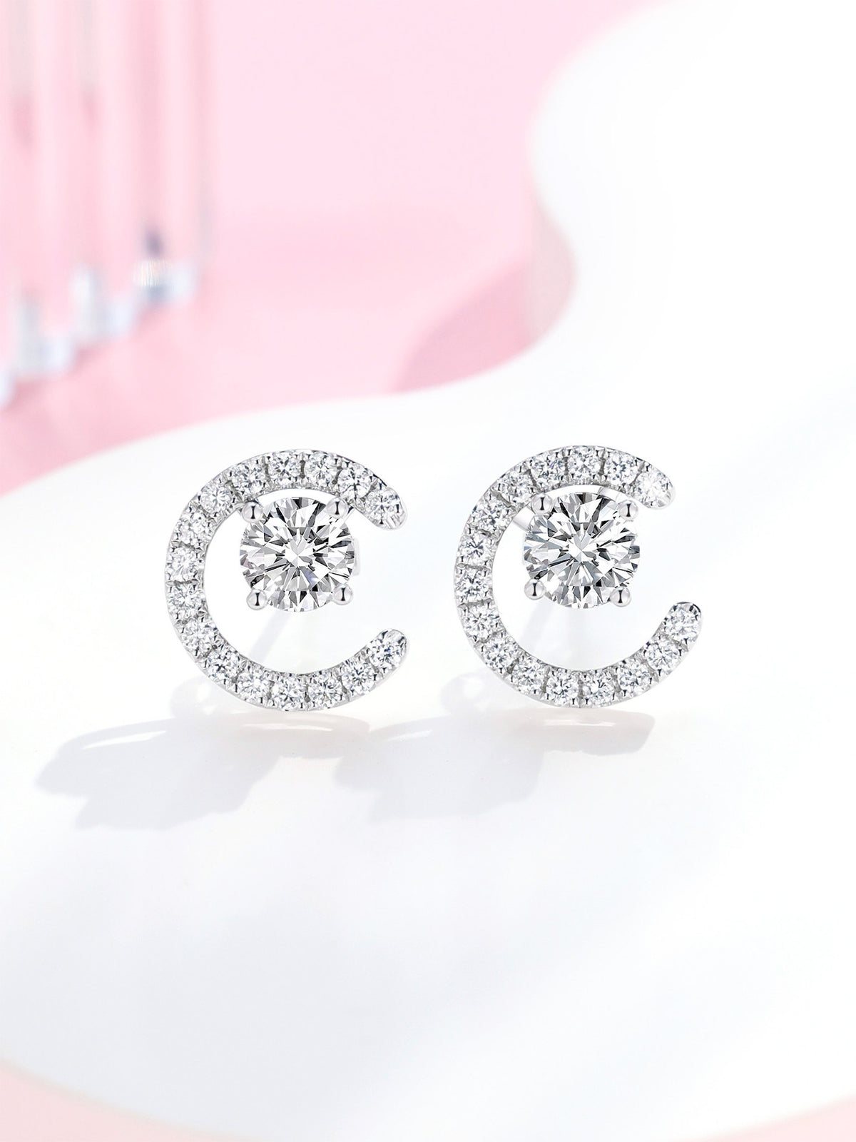 Pair of Lune crescent diamond earrings in platinum on a soft pink and white set