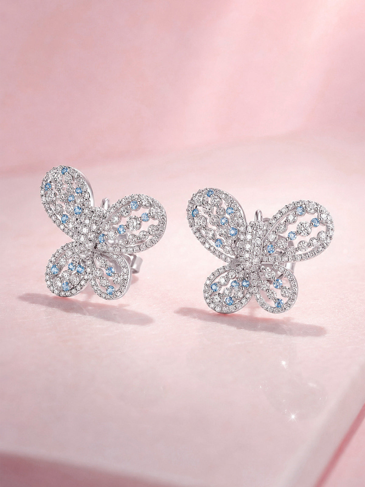 Papillon butterfly diamond stud earrings, angled view on pink marble