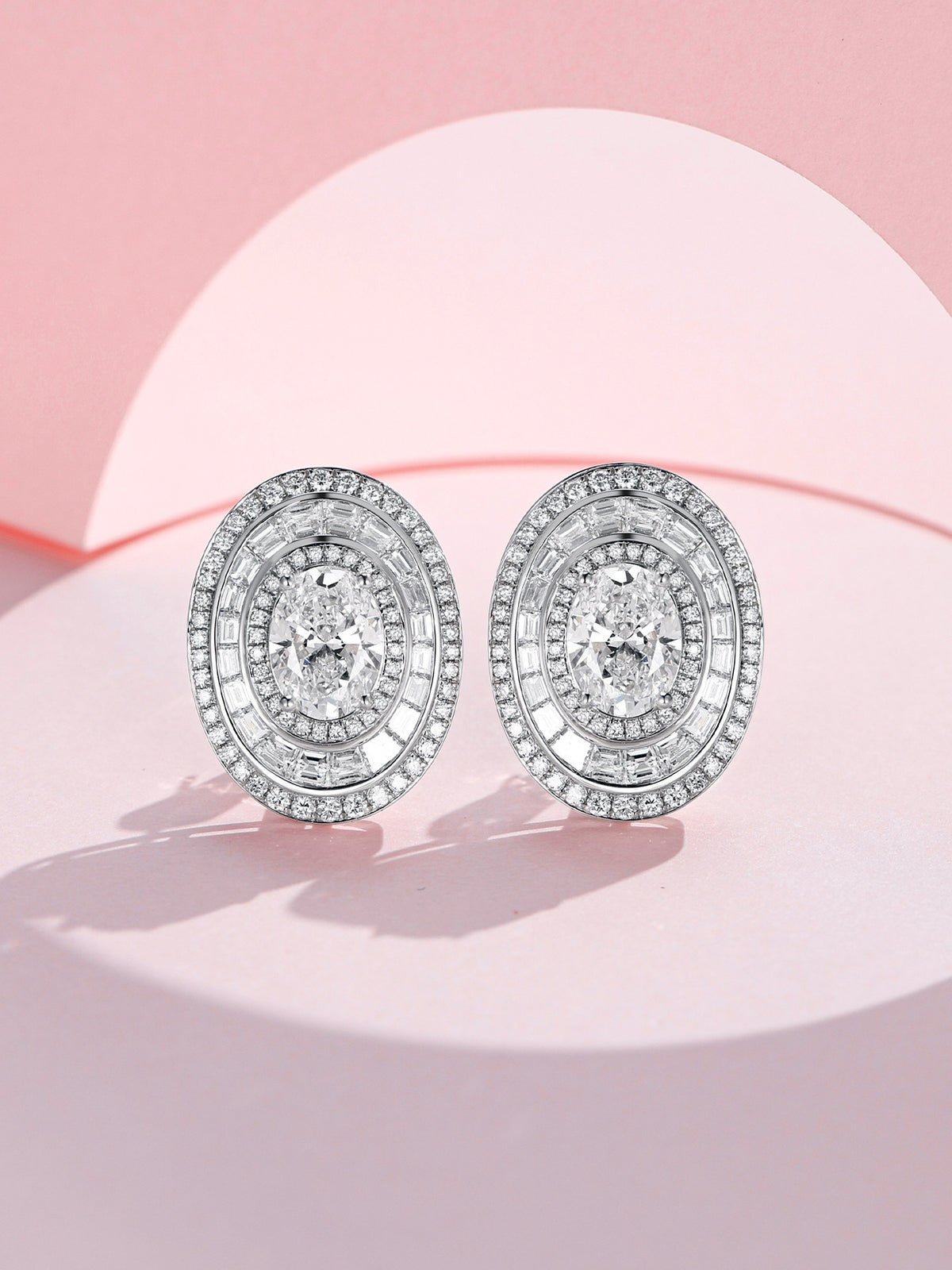 Pair of oval diamond halo earrings in PT950 platinum on a pink backdrop