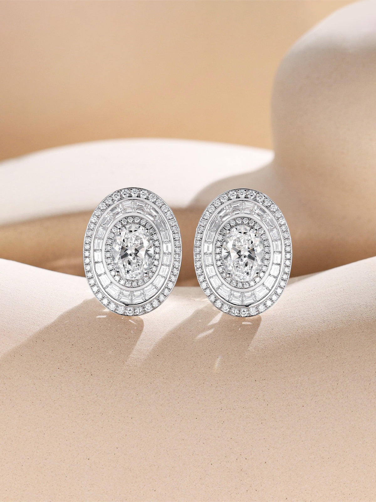 Oval lab-grown diamond halo earrings with baguette ring on a sand-toned set