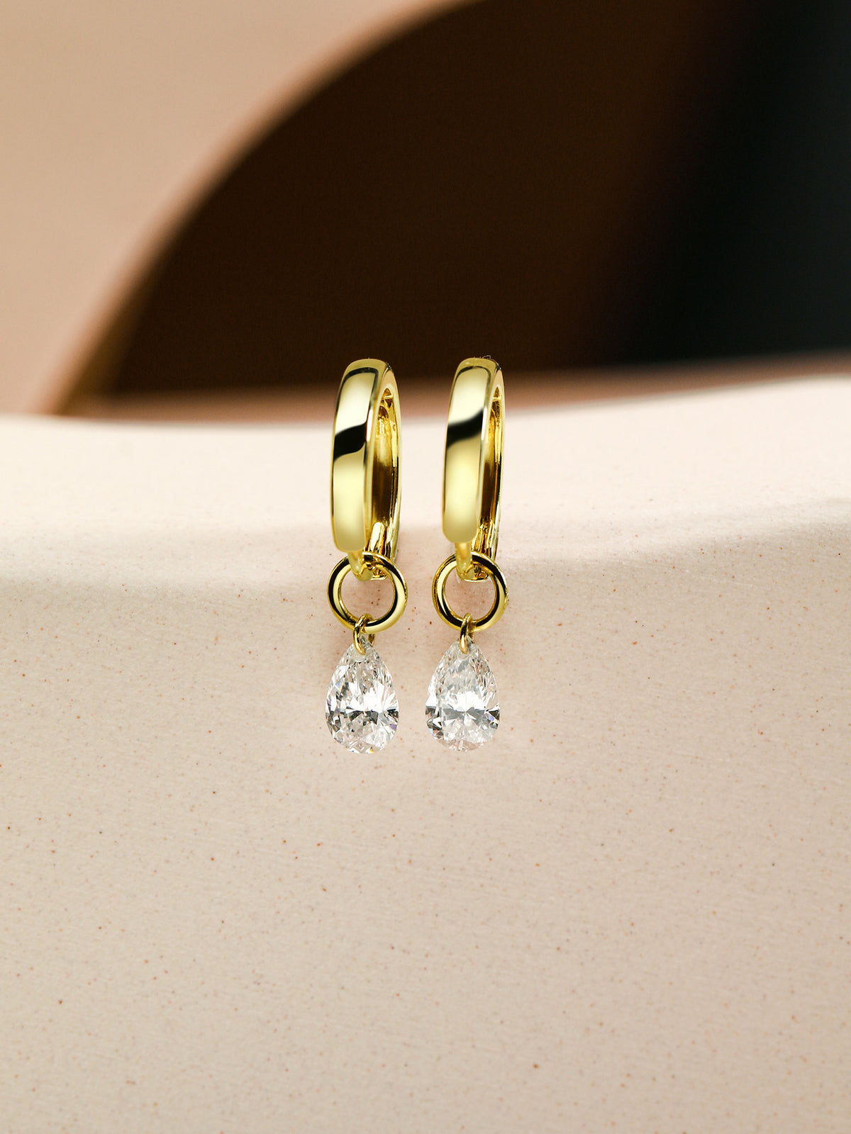 Pear diamond drop huggie earrings in 18K gold on sandstone
