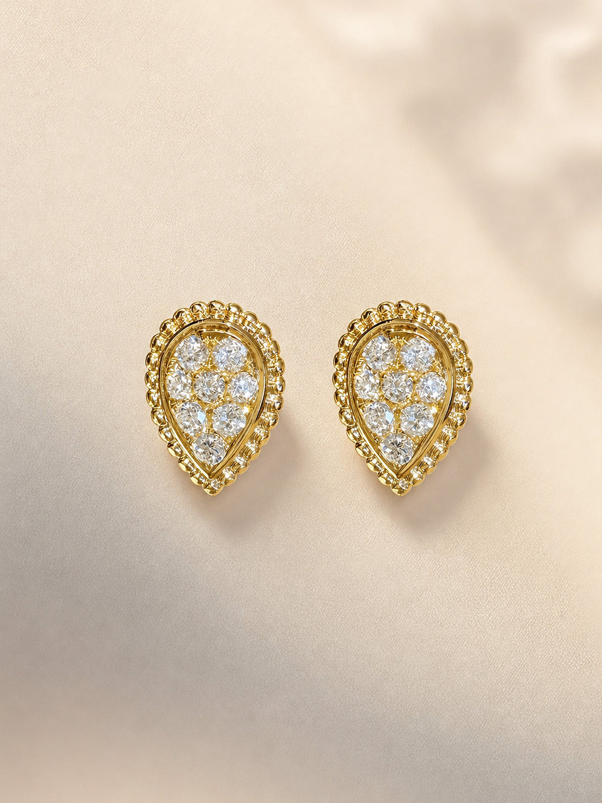 Pear-shaped lab-grown diamond stud earrings with beaded 18K gold frame on ivory satin
