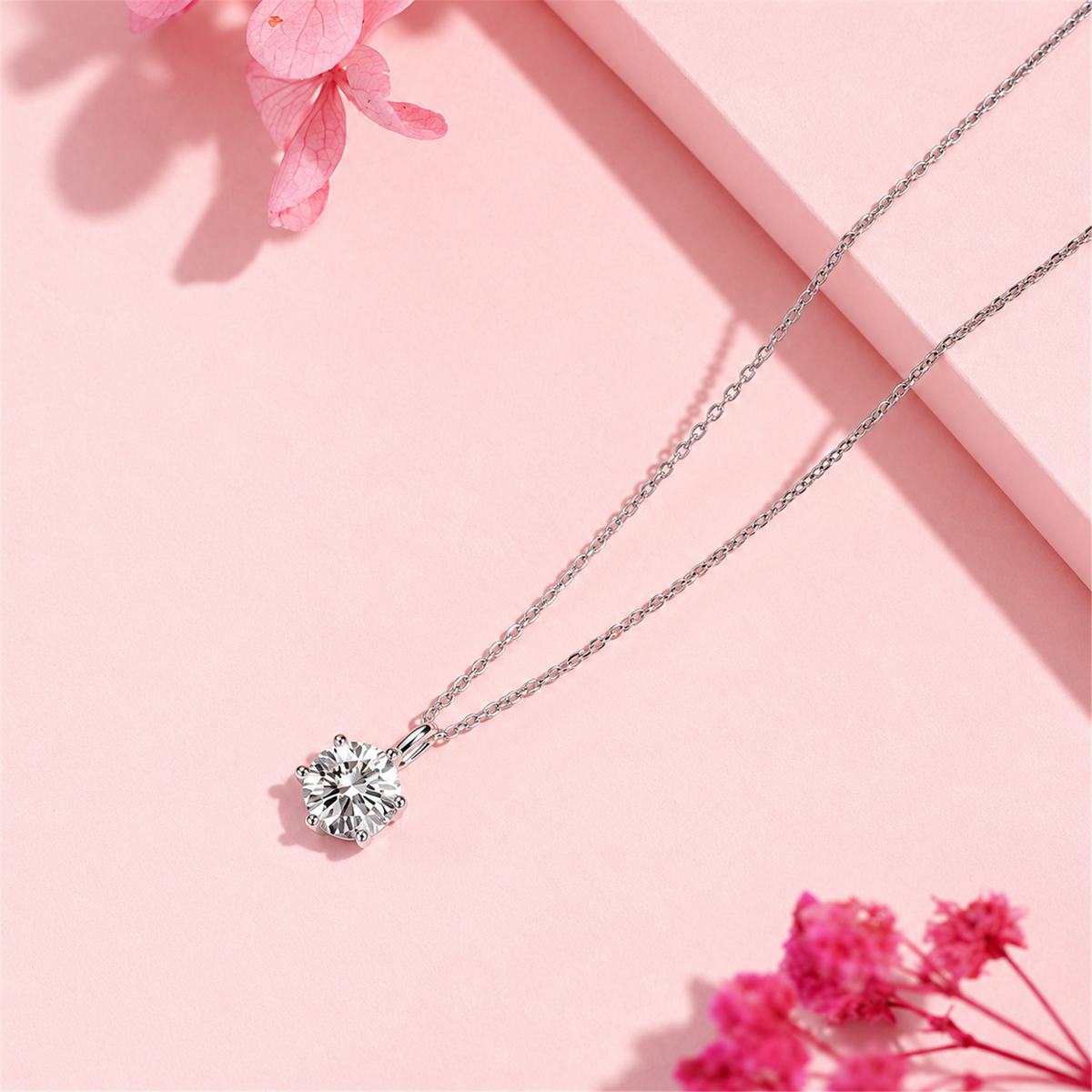 Round solitaire diamond pendant necklace laid diagonally on pink