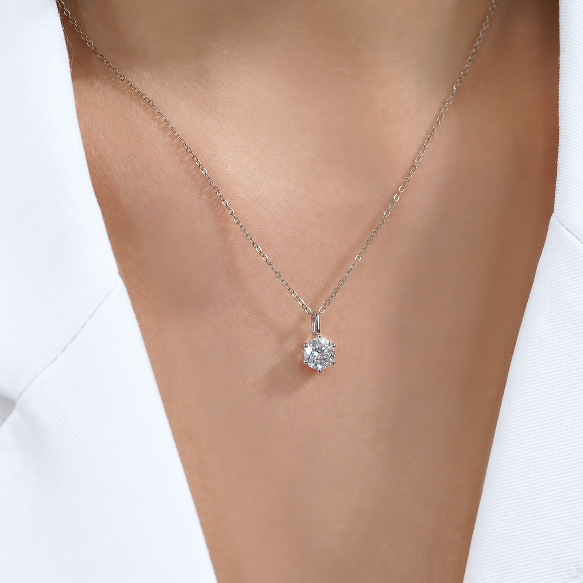 Six-prong diamond pendant necklace worn with white clothing, close-up