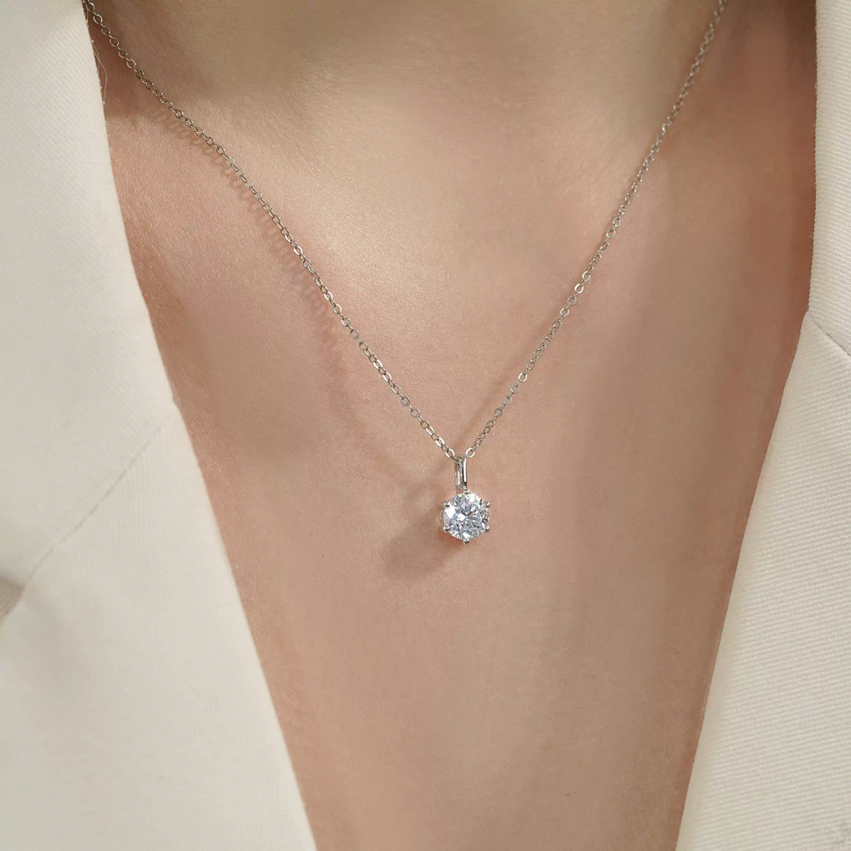 Six-prong diamond pendant necklace worn with white clothing, close-up