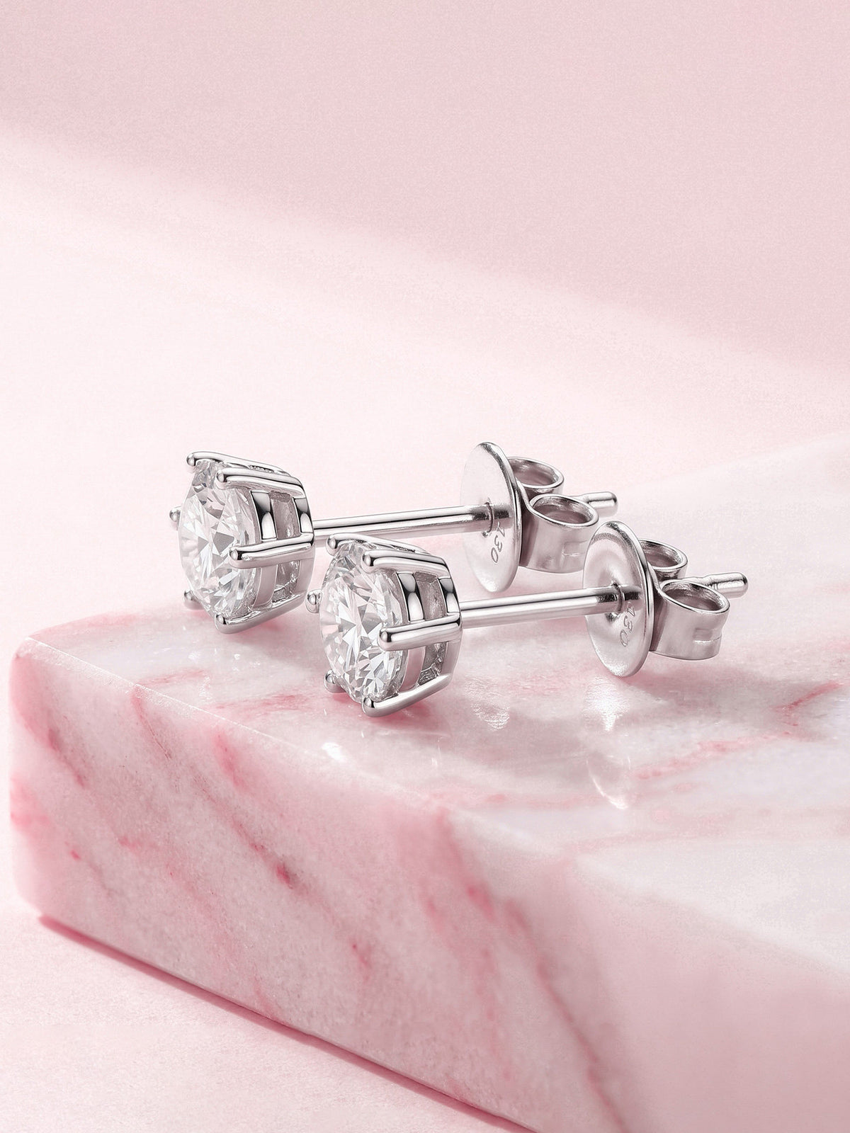 Round lab-grown diamond solitaire studs in 18K white gold on pink marble