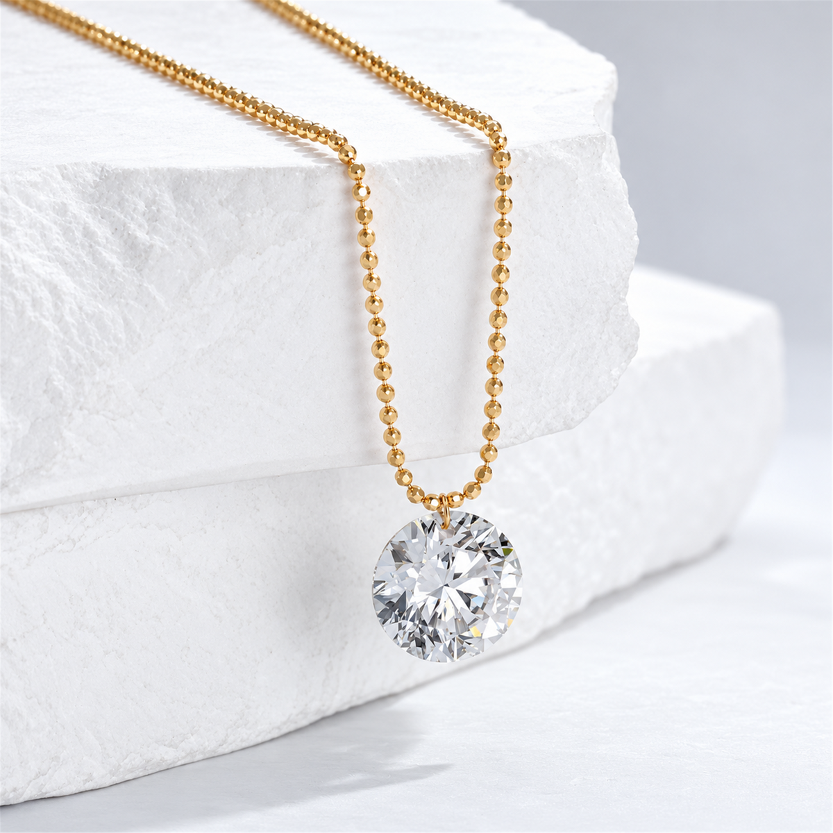 Yellow gold bead chain and round diamond pendant on a white stone display; digitally retouched supplier image