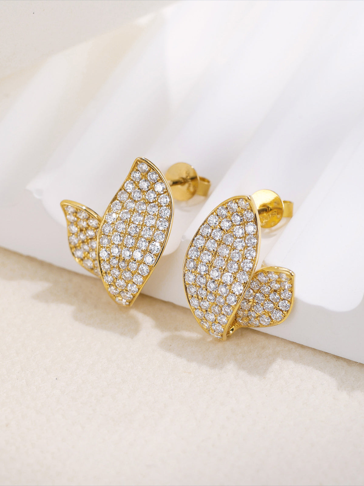 Pair of 18K gold pavé leaf diamond stud earrings on white display stand