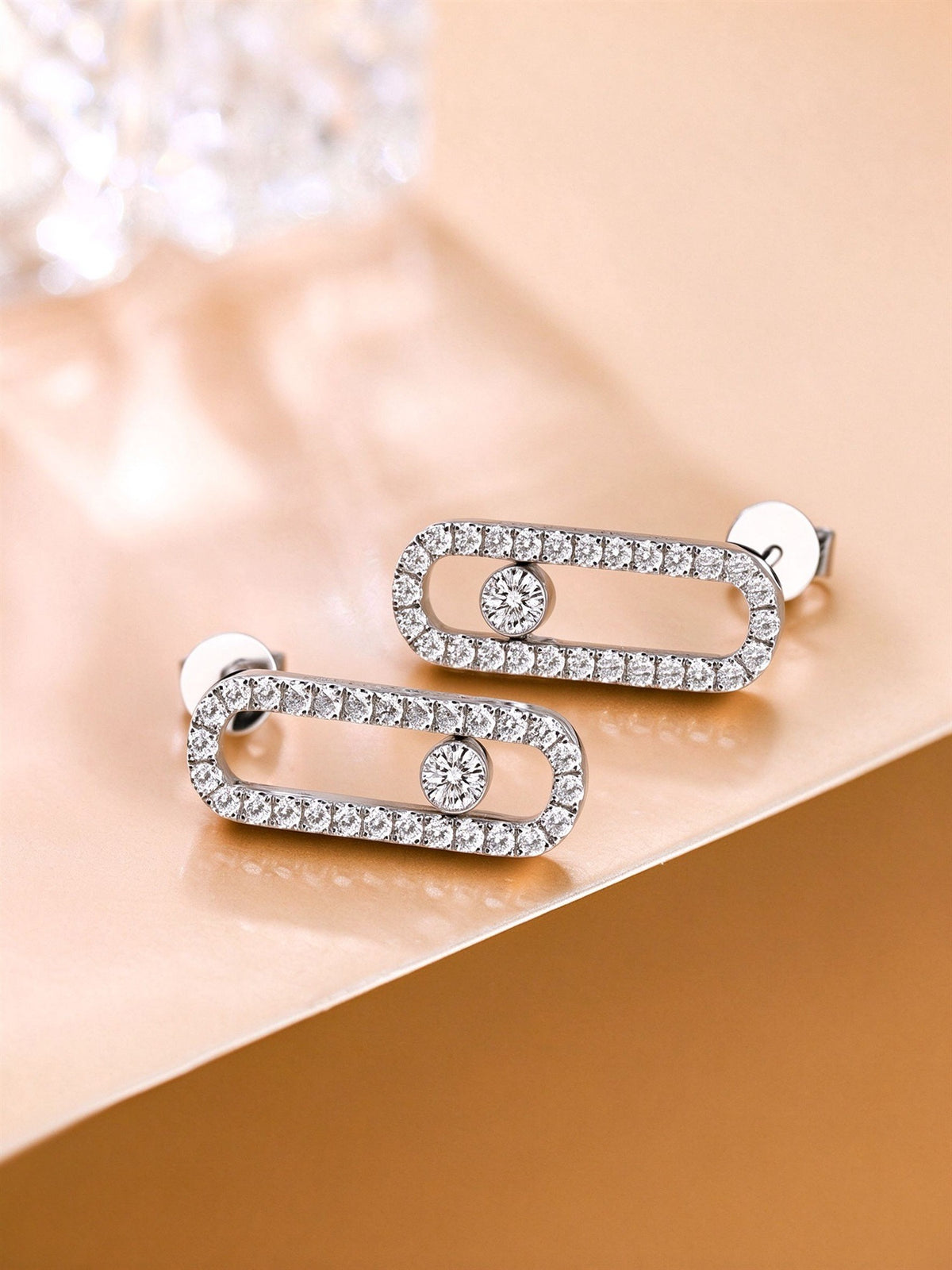 Pavé diamond paperclip stud earrings with bezel-set centre stone on warm gold card