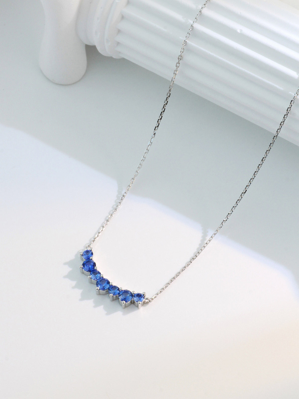 DANFÉE Seven-Stone Smile sapphire necklace on a white sculpted column