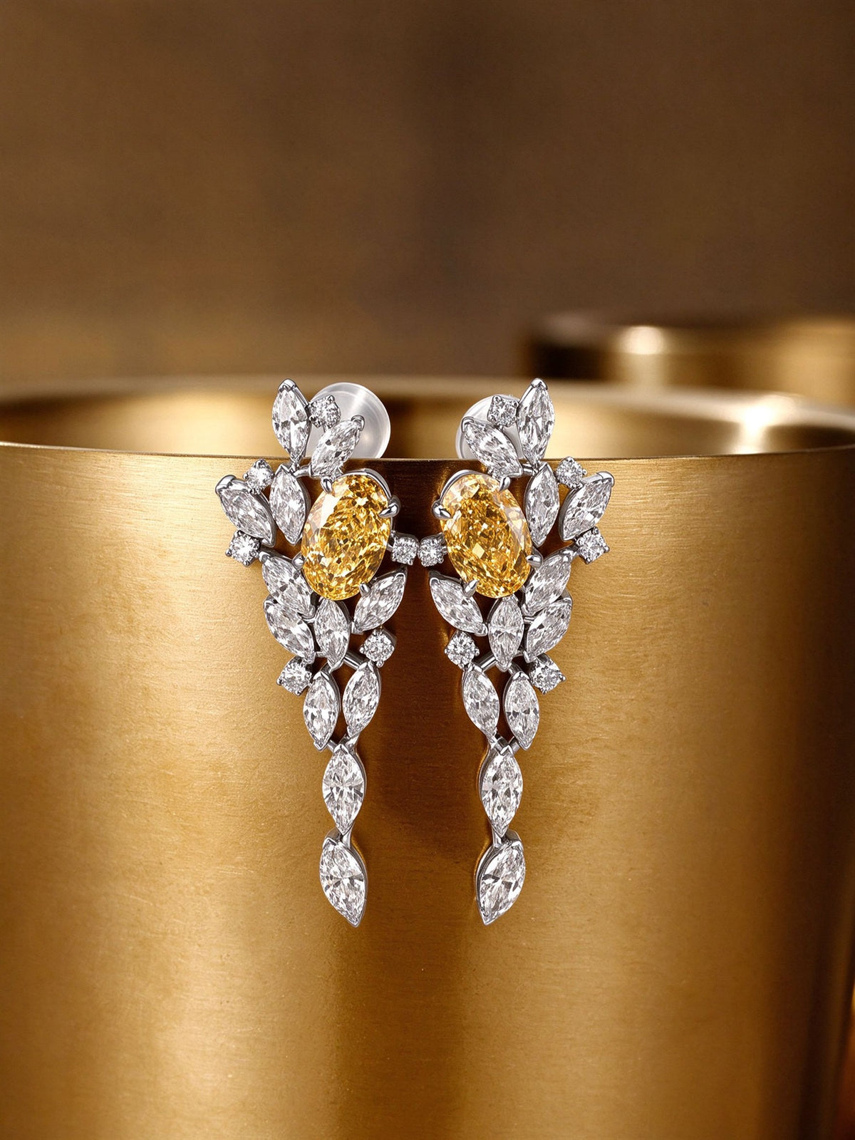 Pair of oval yellow lab-grown diamond drop earrings displayed on brushed gold